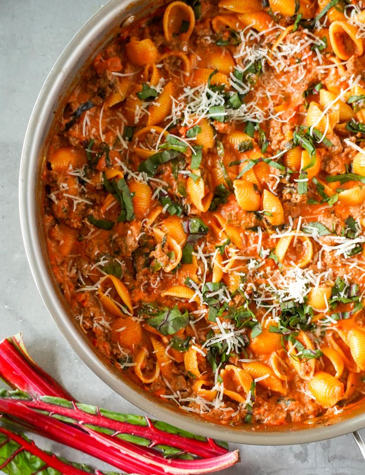 a pot filled with pasta and sauce on top of a table next to red radishes