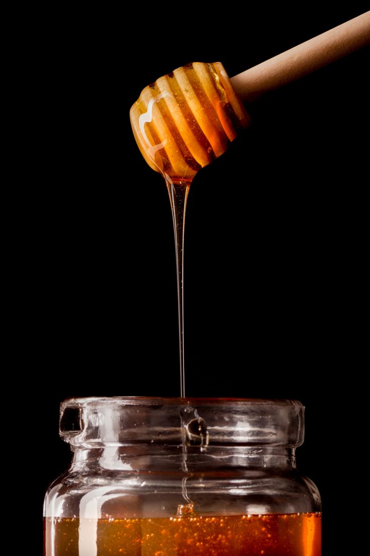 a honey dip is being poured into a glass jar filled with honey and topped with a wooden stick