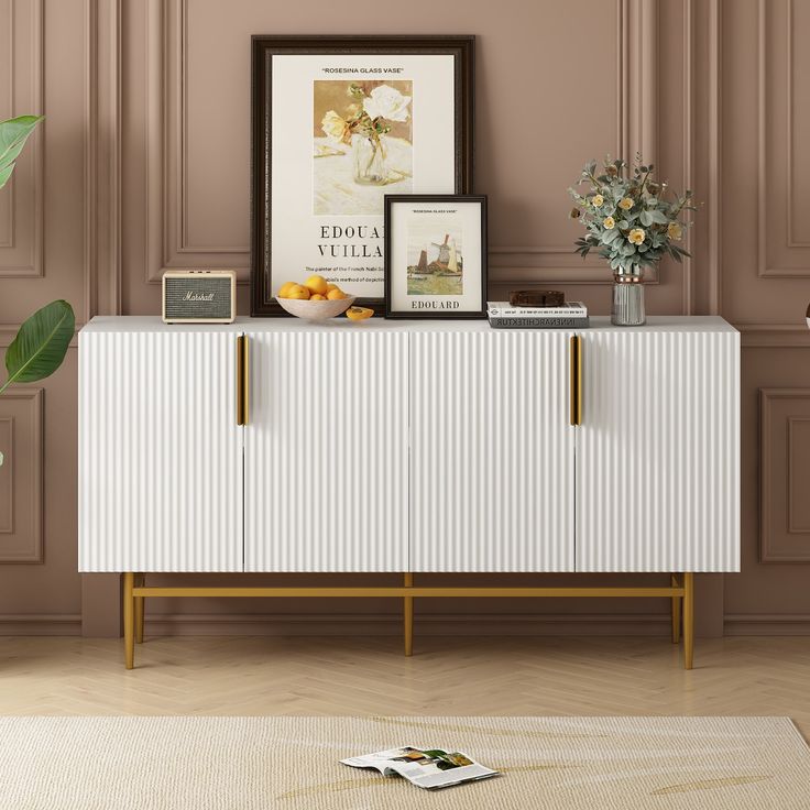 a white cabinet sitting in the corner of a room next to a plant and pictures