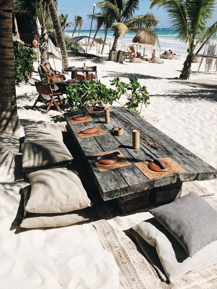 a picnic table set up on the beach with plates and utensils laid out