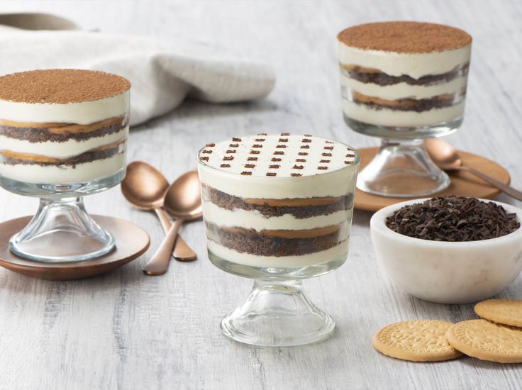 three desserts are sitting on the table with spoons next to them and cookies