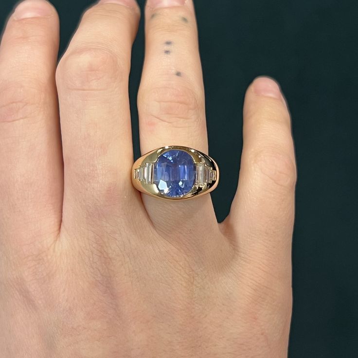 This cocktail ring features a flush set blue sapphire and diamonds in polished 14 karat yellow gold. An impressive 7.24 carat Cornflower Blue Sapphire. A collection of baguette diamonds flank the center stone. The sparkling gems are set flush and secure on a thick, 14mm wide band. Make a bold statement this season with this gorgeous cocktail ring! Modern stylish. An unforgettable statement ring for everyday elegance. Luxury Gold Sapphire Ring With Recycled Gold, Luxury Gold Sapphire Ring With Polished Finish, Luxury Gold Sapphire Ring For Collectors, Sapphire Diamond Rings, Vintage Gold Sapphire Ring, Cocktail Ring, Colored Stone Engagement Rings, Sapphire Cocktail Ring, Radiant Cut Engagement Rings