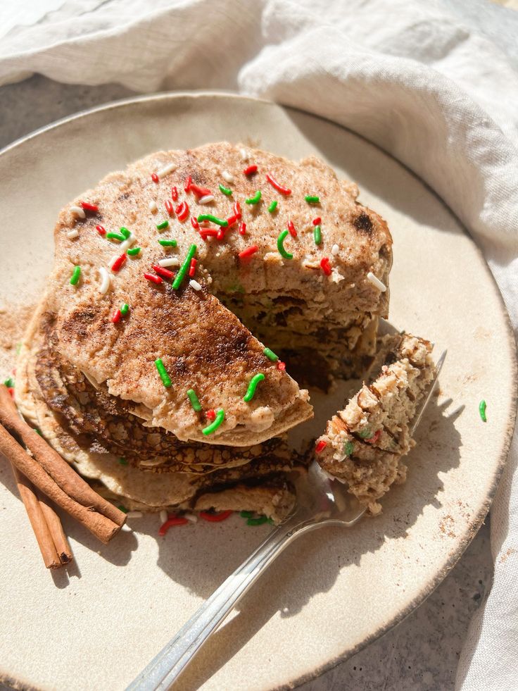 a stack of pancakes with sprinkles and cinnamon sticks on a white plate