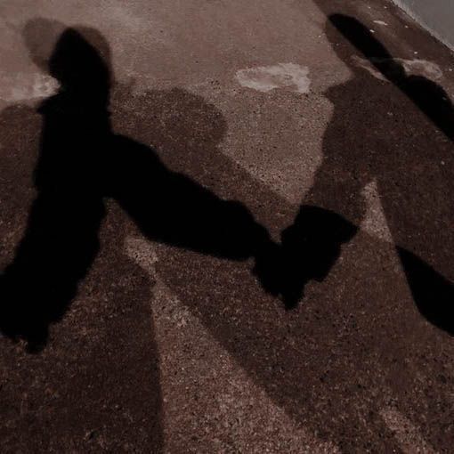 the shadow of two people holding hands walking down a street with a stop sign in the background