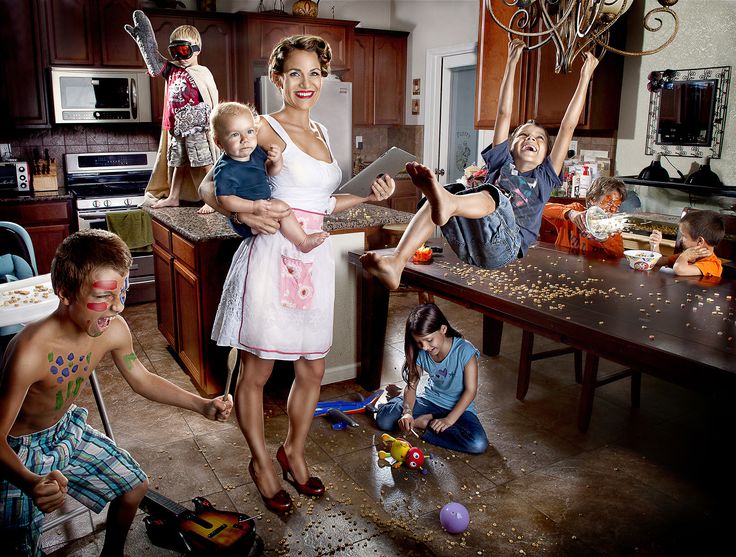 a group of people standing in a kitchen with one woman holding a baby and two children