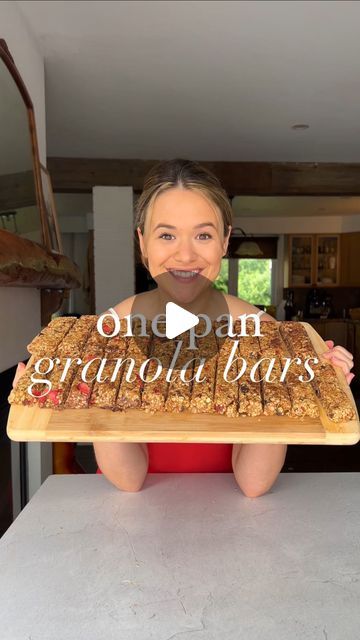 a woman sitting on top of a counter holding a wooden tray with granola bars