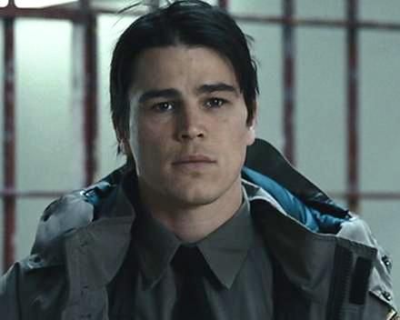 a young man wearing a jacket and tie in front of a caged area with bars