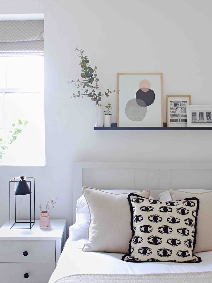 a bedroom with white walls, black and white pillows and pictures on the wall above the bed