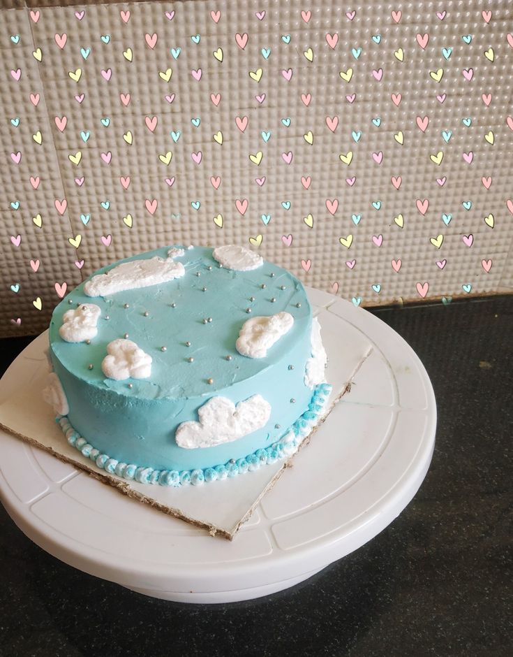 a blue cake sitting on top of a white plate next to a wall with hearts