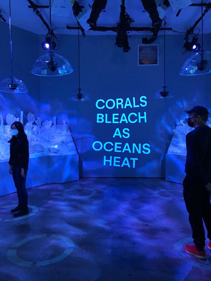 two people standing in front of a blue wall with words on it that read corals bleach as oceans heat