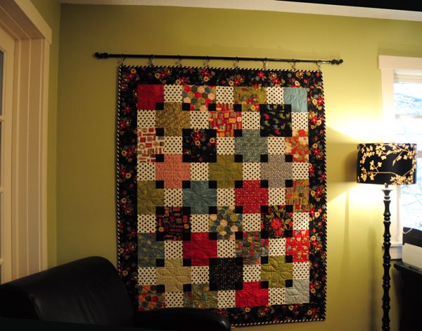 a quilt hanging on the wall next to a chair and lamp in a living room