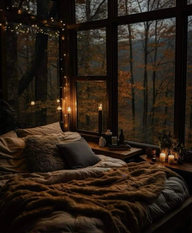 a bed with blankets and candles on it in front of a window that looks out onto the woods