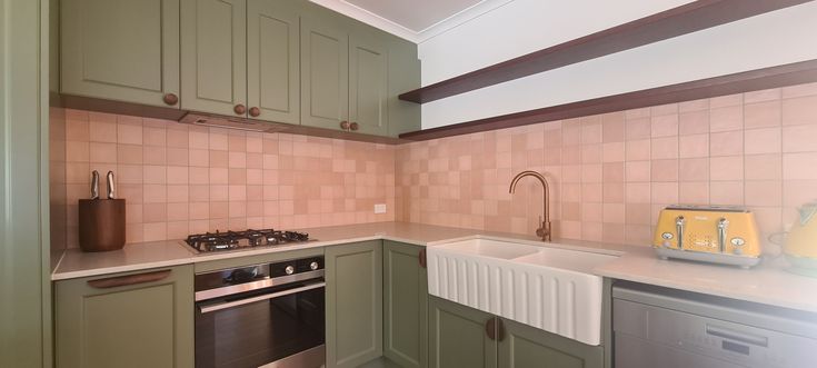 a kitchen with green cabinets and pink tile backsplash, white countertops and stainless steel appliances