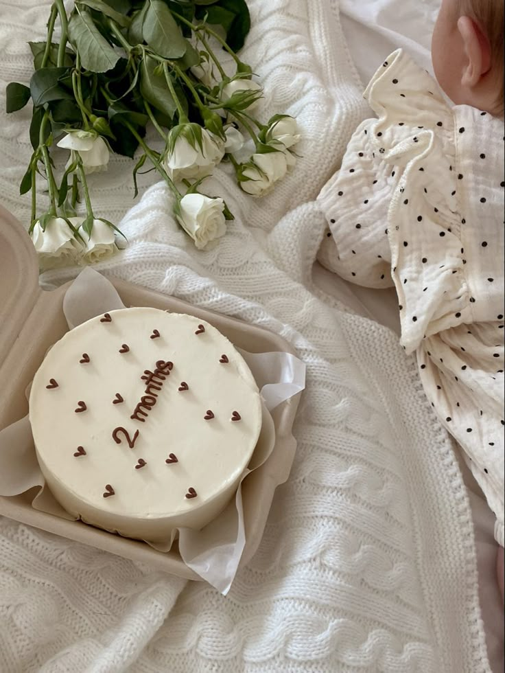 a baby laying on top of a bed next to a cake