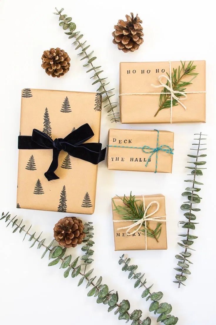 christmas presents wrapped in brown paper and tied with black ribbon, surrounded by pine cones