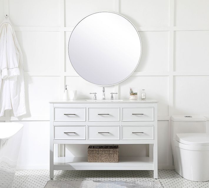 a white bathroom with a round mirror above the sink