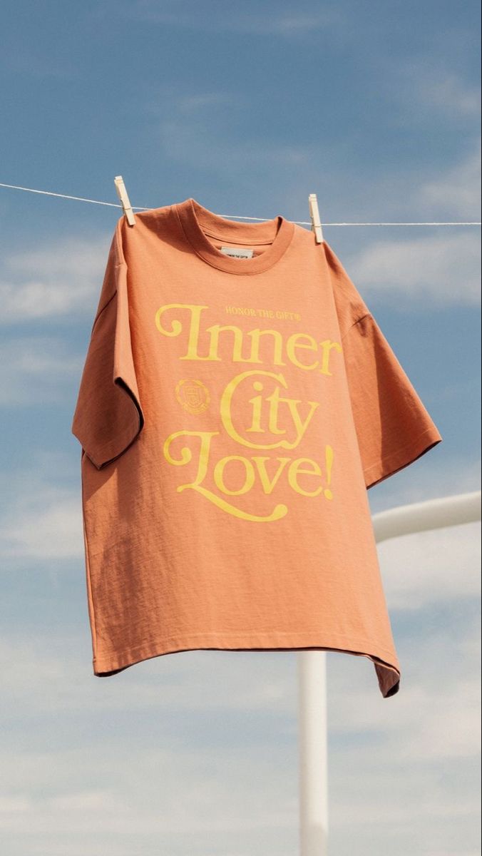 an orange t - shirt that says inner city love hangs on a clothes line against a blue sky