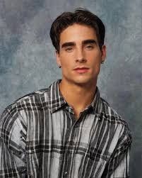 a young man wearing a plaid shirt posing for a photo in front of a blue background