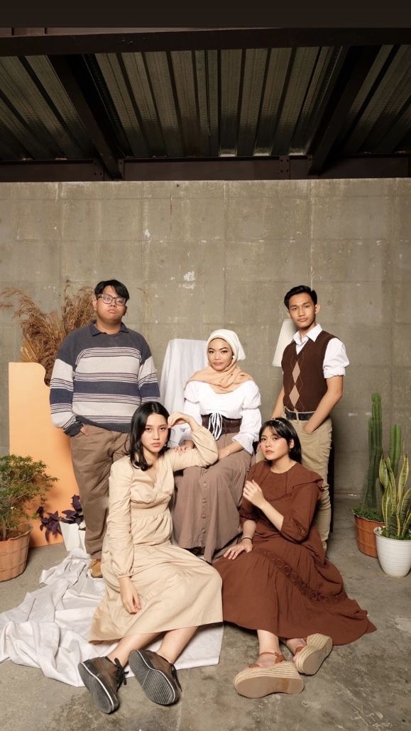 a group of people sitting next to each other in front of a cement wall and potted plants