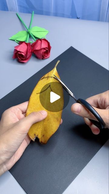 someone cutting up a leaf with scissors on top of a piece of paper next to flowers