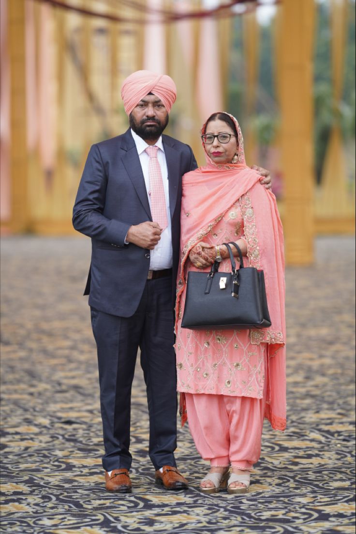 two people standing next to each other wearing suits and turbans, one holding a handbag