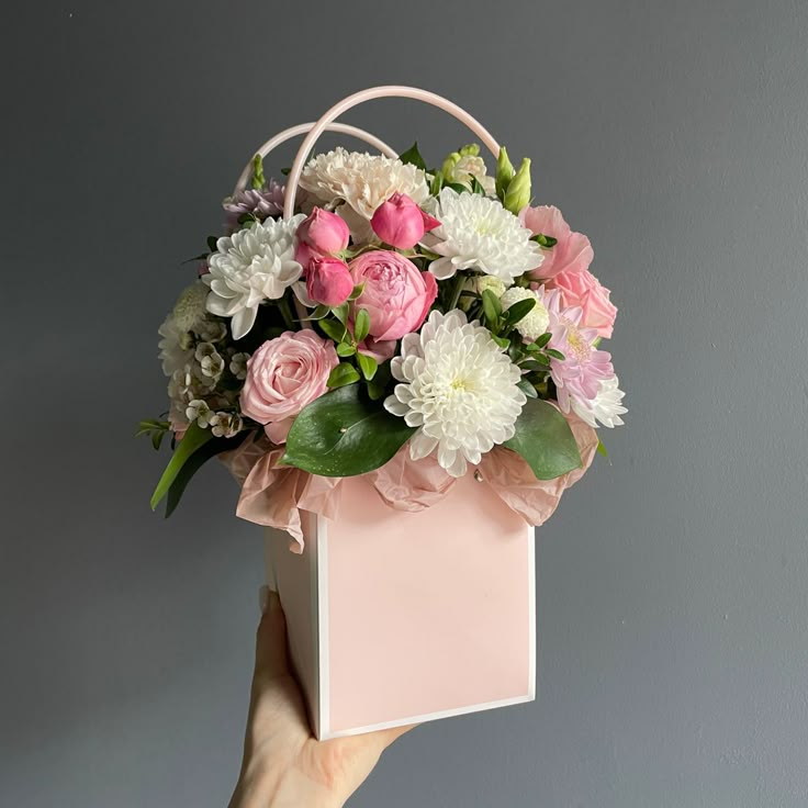 a hand holding a pink and white flower box