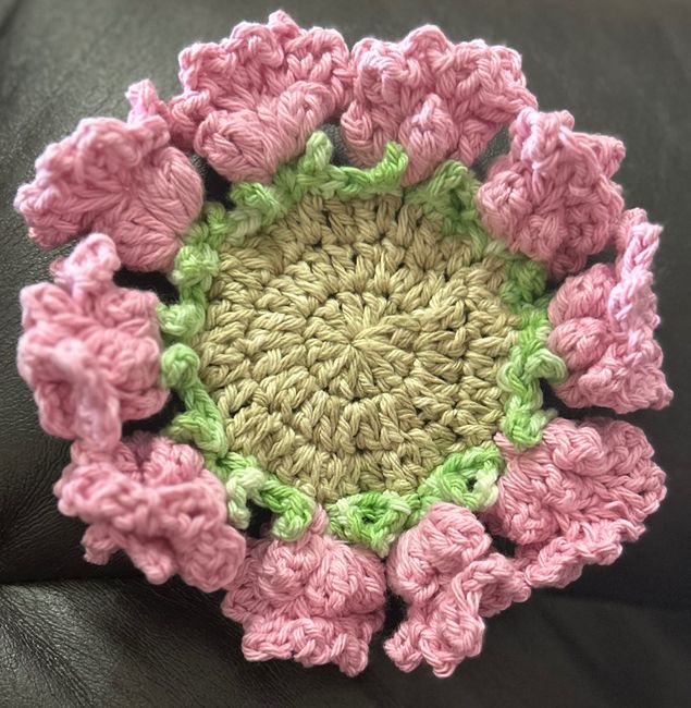 a crocheted pink and green flower sitting on top of a black couch