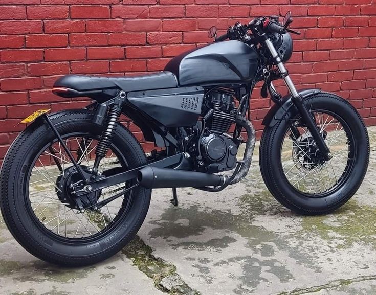 a black motorcycle parked in front of a brick wall