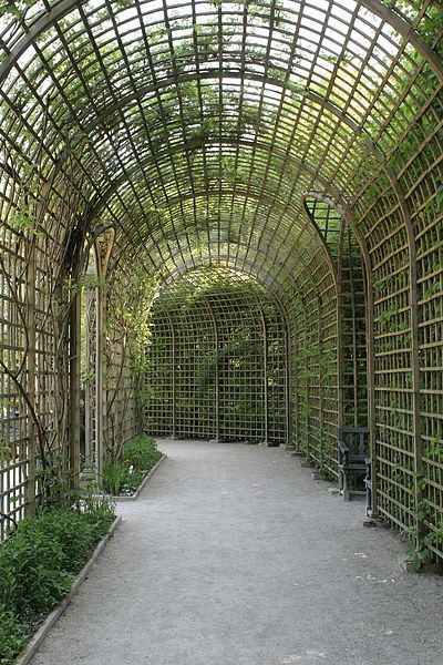 the walkway is lined with green plants and wooden latticed structures that are all over the place