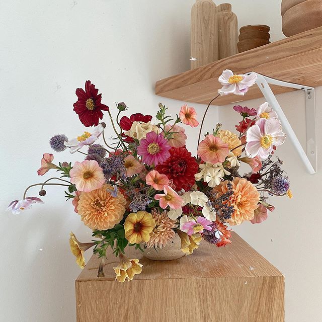 a vase filled with lots of colorful flowers on top of a wooden table next to a shelf