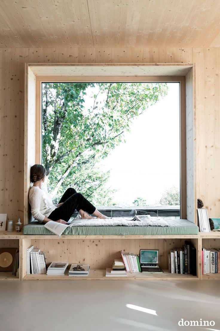 a woman sitting on a bed in front of a large window with bookshelves