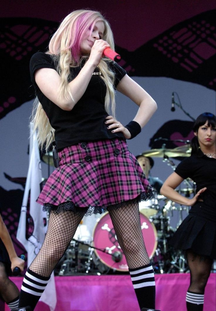 a woman with pink hair and black stockings is on stage holding a microphone in her hand