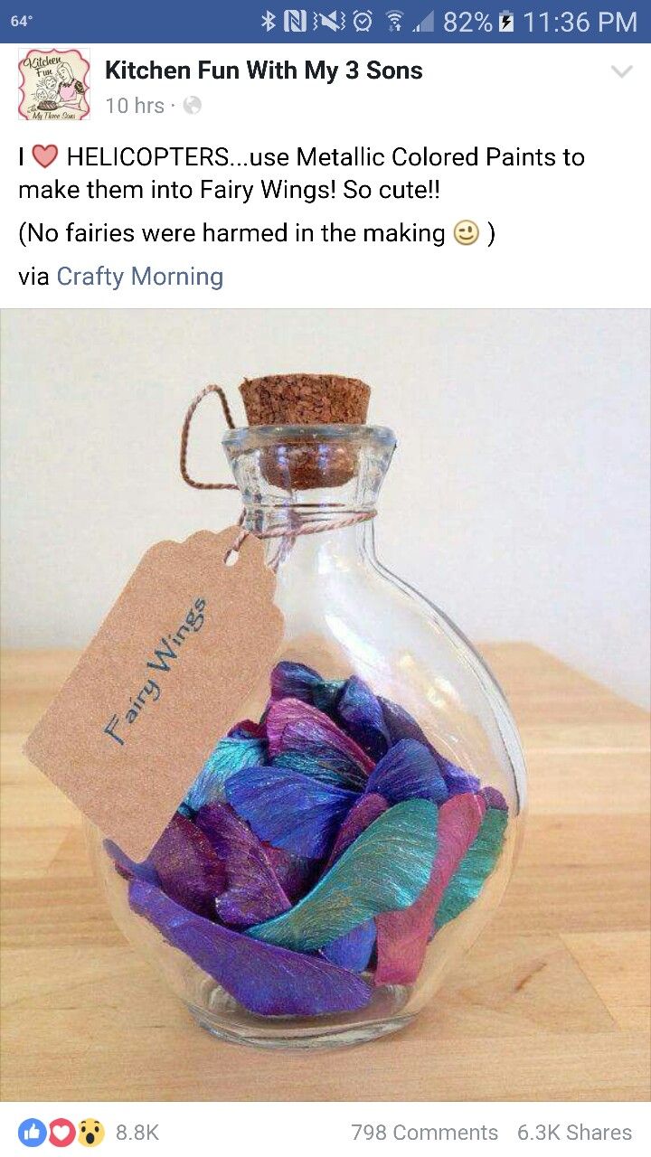 a glass bottle filled with purple and blue feathers on top of a wooden table next to a tag