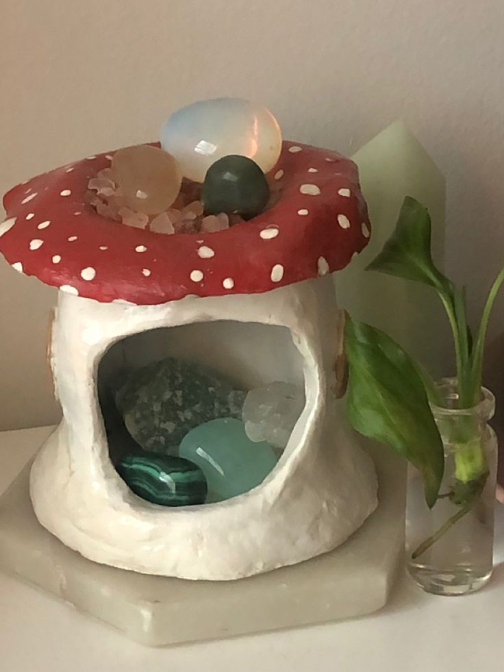 there is a small mushroom house on the table next to a vase with flowers in it