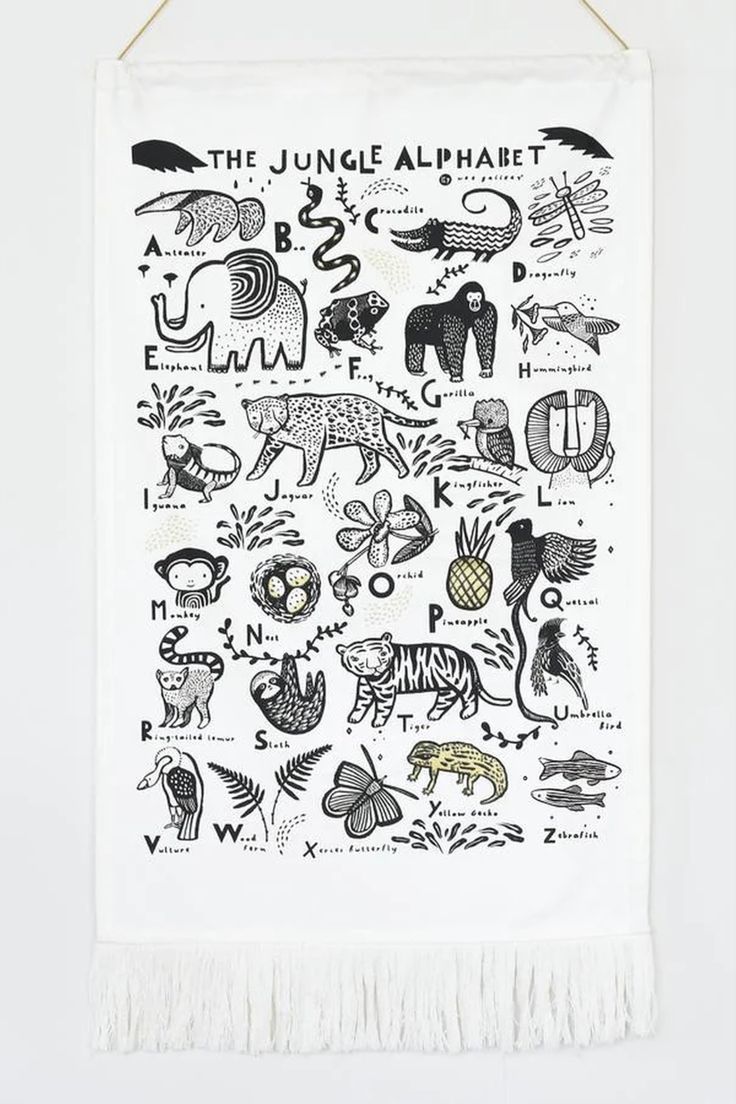 the jungle alphabet tea towel hanging on a white wall with black and white images in it