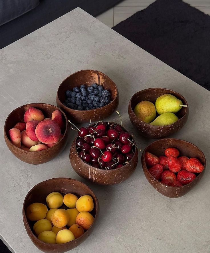 five bowls filled with different types of fruit on top of a white countertop next to a couch