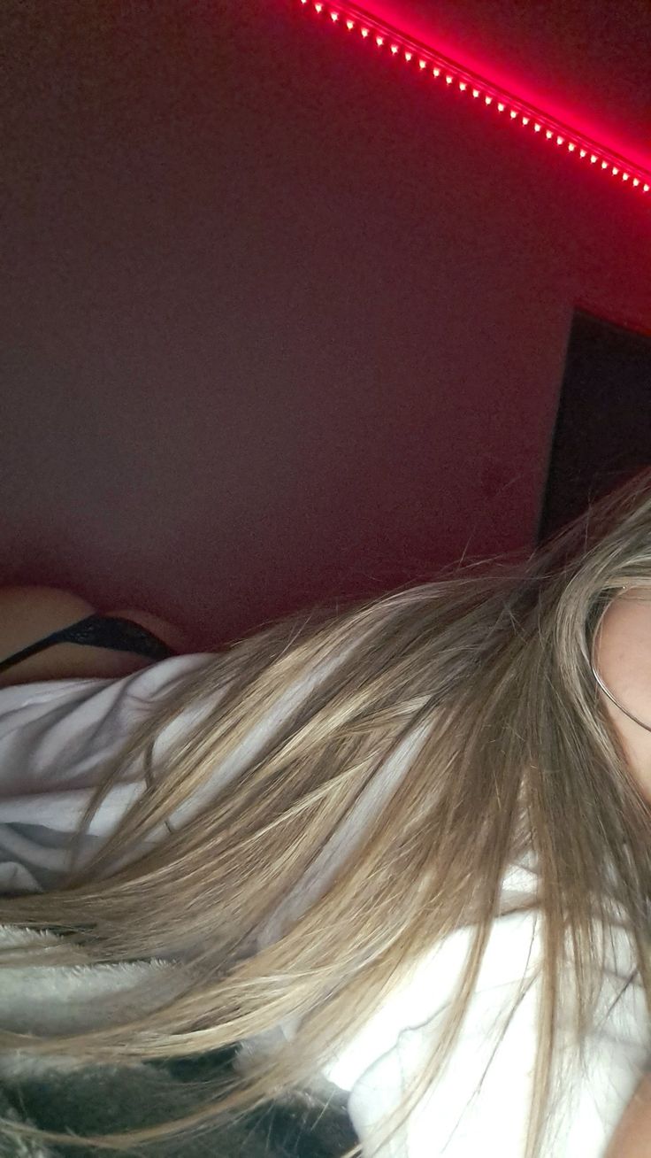 a woman with long blonde hair laying on top of a bed next to a red light