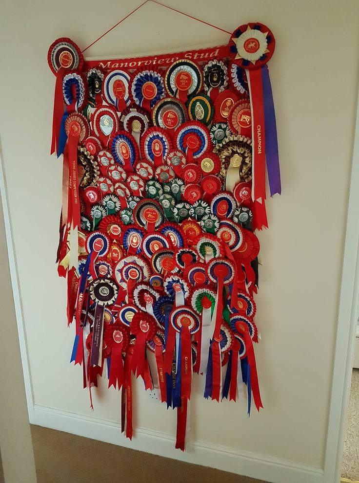 a wall hanging made out of ribbons and other items on a white wall with a door in the background