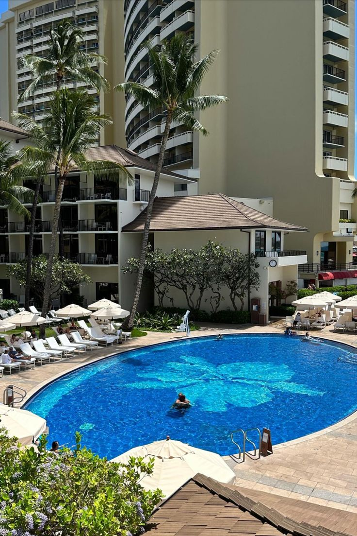 an outdoor swimming pool with lounge chairs and palm trees in the background, surrounded by tall buildings