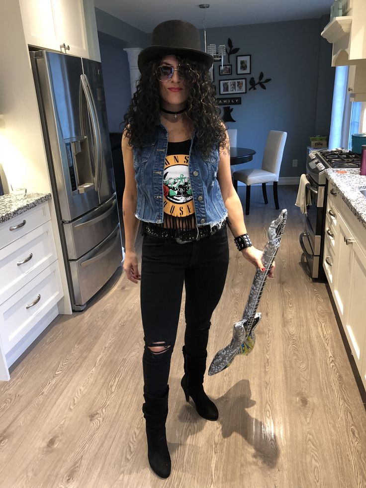 a woman standing in a kitchen holding a large metal hammer and wearing a black hat