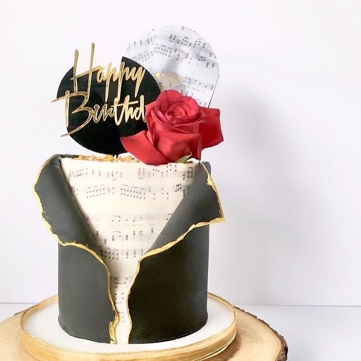 a birthday cake decorated with music notes and a red rose sits on top of a piece of wood