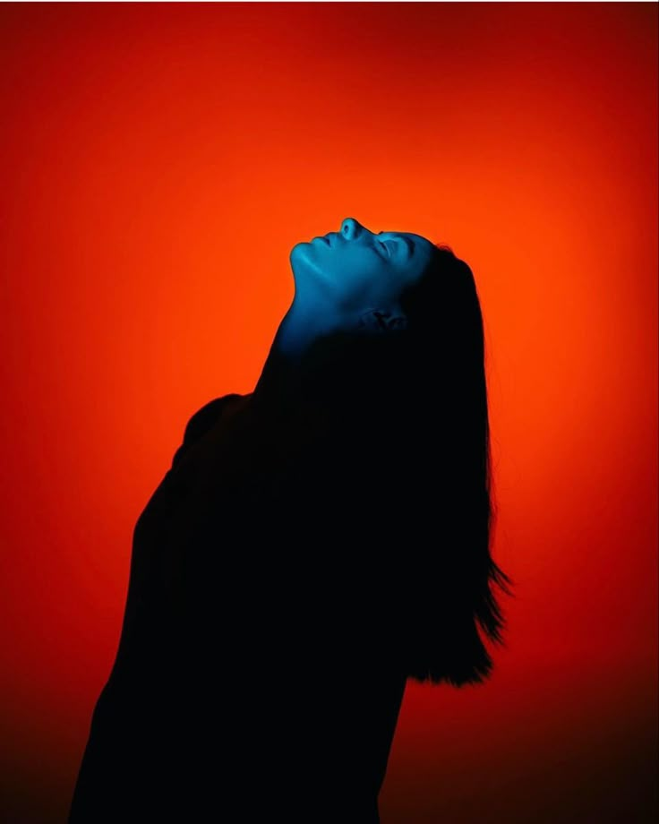 the silhouette of a woman with her eyes closed in front of an orange and red background