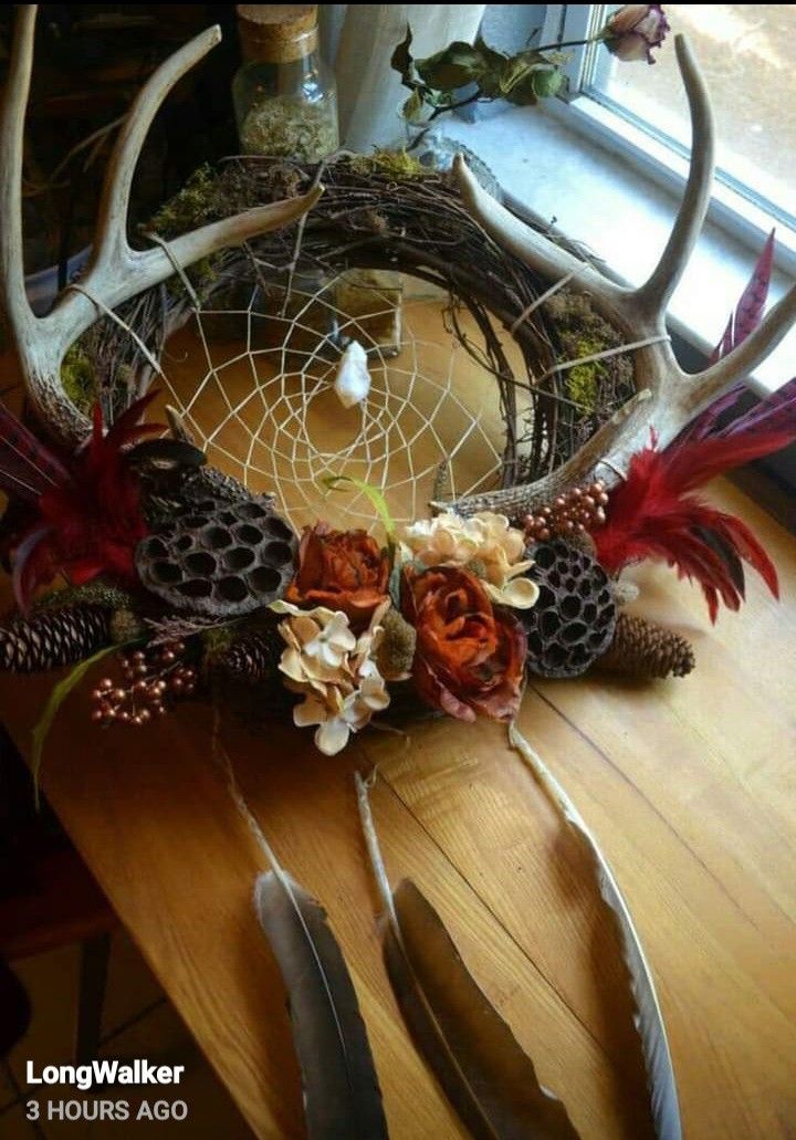 an antler with flowers and feathers on top of a wooden table next to a window