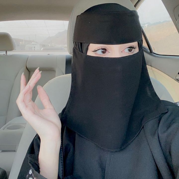 a woman wearing a black hijab holding her hand up in front of her face