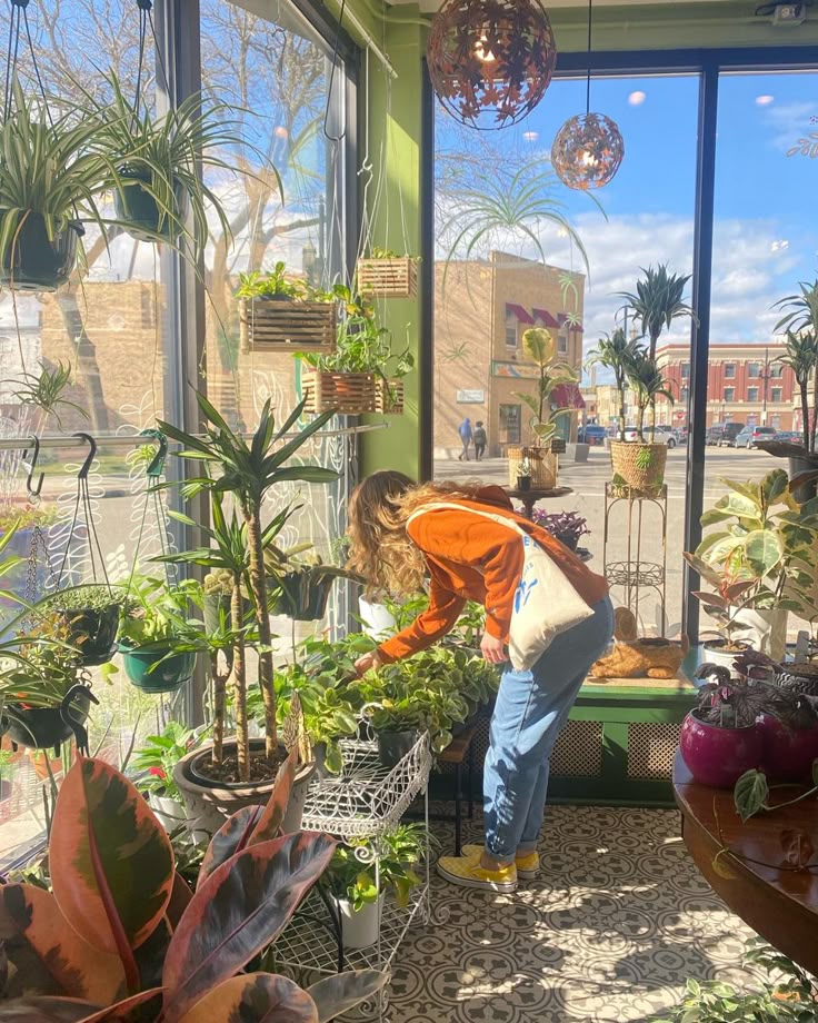 a woman tending to plants in a room with large windows and lots of potted plants