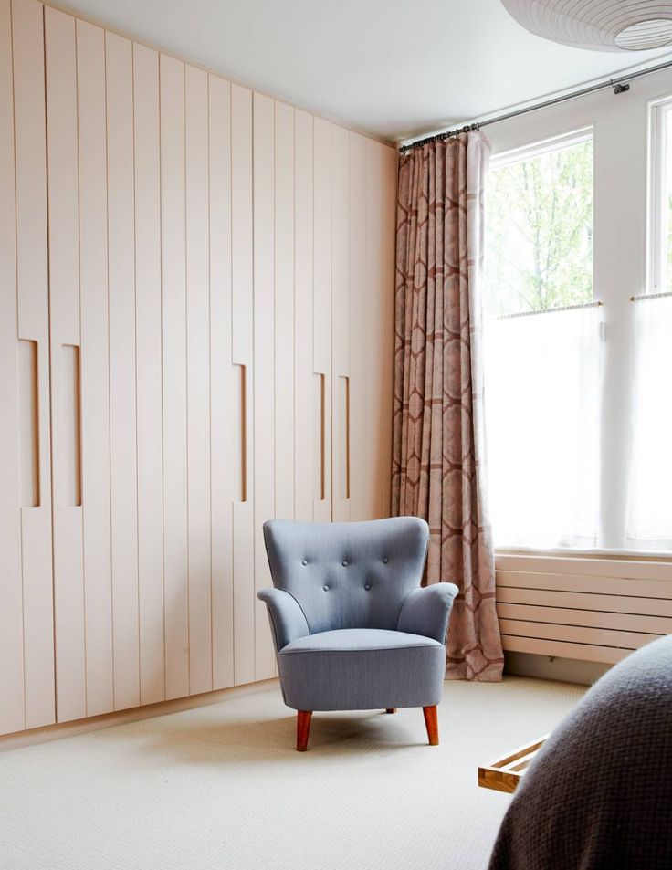 a blue chair sitting in front of a window next to a white dresser and bed