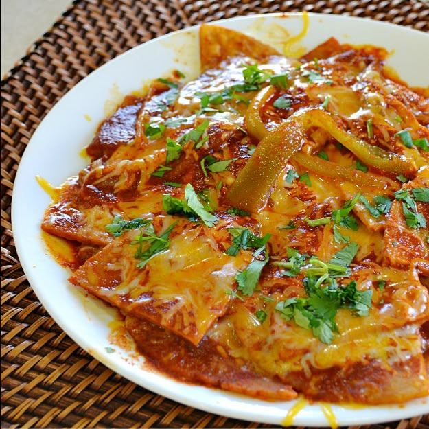 a white plate topped with lasagna covered in sauce and green garnish