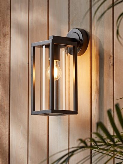 an outdoor light on the side of a wooden wall next to a potted plant