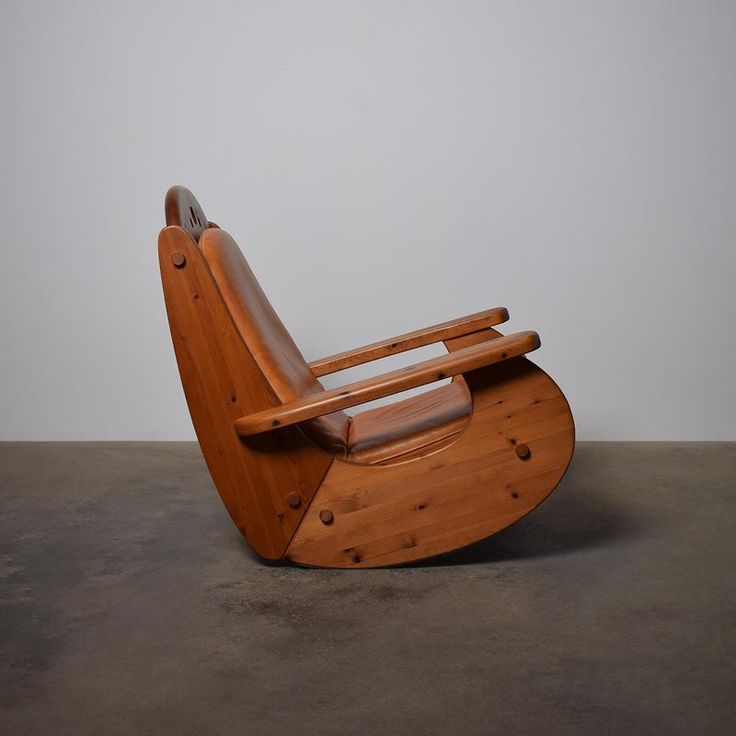 a wooden rocking chair sitting on top of a cement floor next to a white wall