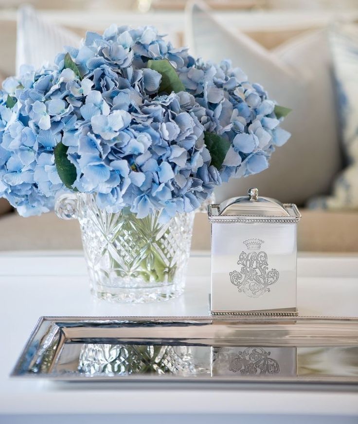 blue hydrangeas in a glass vase on a tray next to a silver mirror